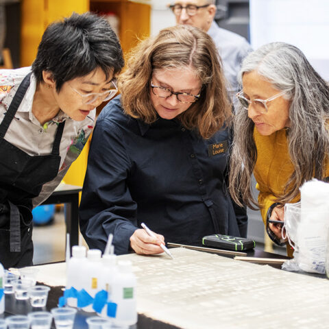 Three female conservators lean in to view a cleaning process during a modular cleaning programme workshop hosted in the Carlisle studio