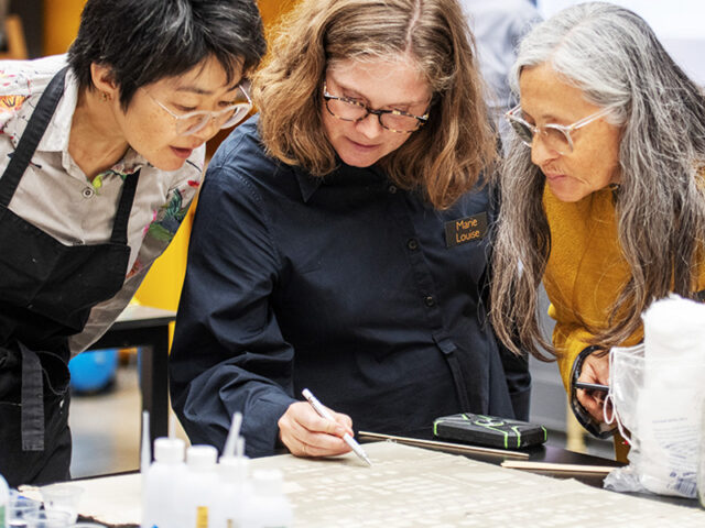 Three female conservators lean in to view a cleaning process during a modular cleaning programme workshop hosted in the Carlisle studio