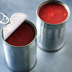Two open cans of soup with tomato soup inside